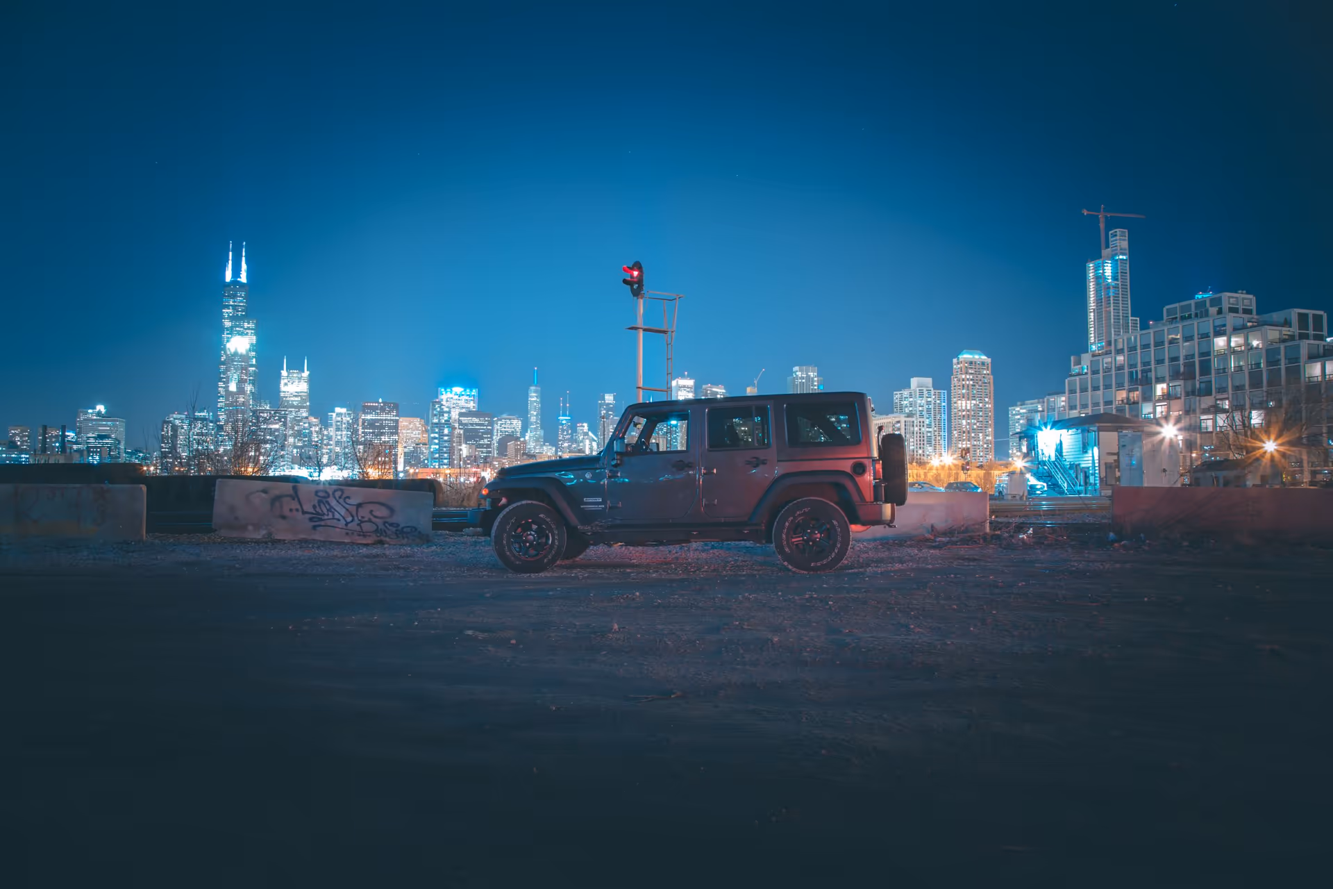 A Jeep parked on a gravel lot at night with the Chicago skyline behind it