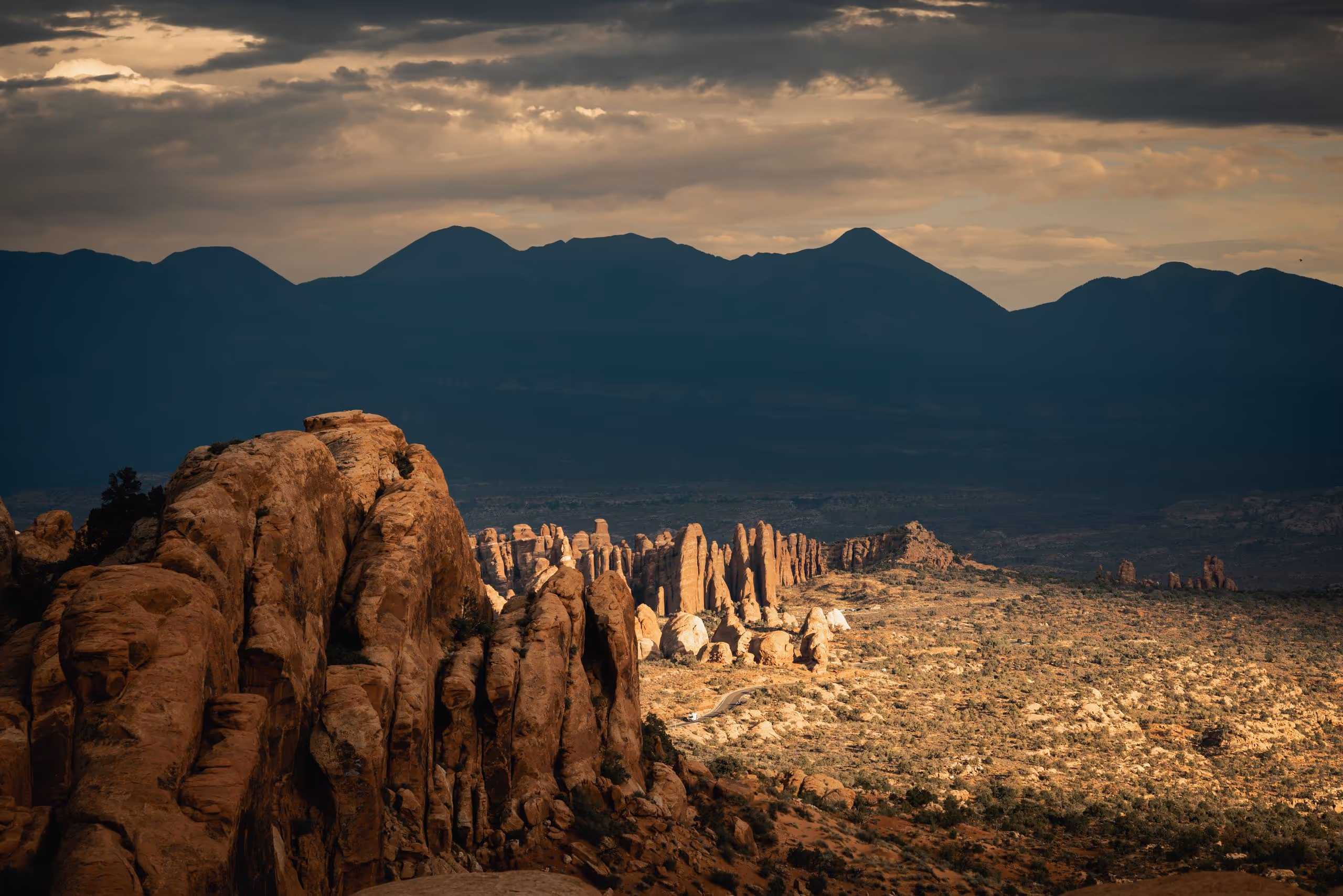 Sandstone spires and ridges in the Utah desert at sunset, with a mountain range behind